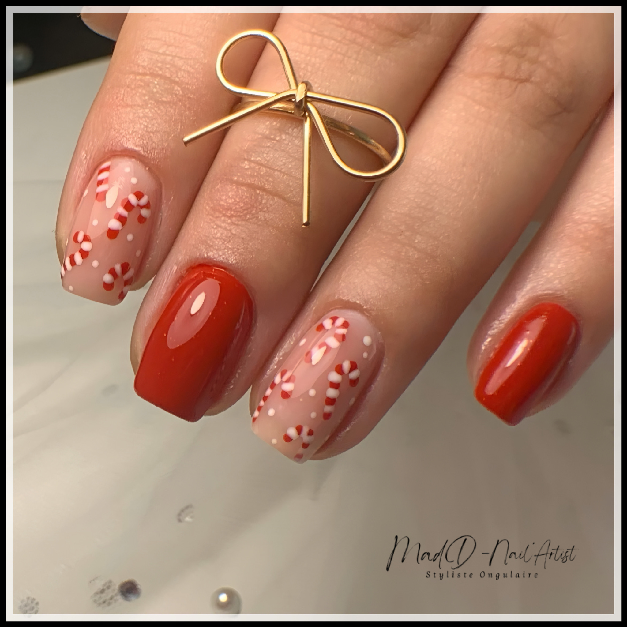 Nail art de Noël avec bonbons candy cane rouges et blancs sur fond nude, combiné à des ongles rouges brillants.