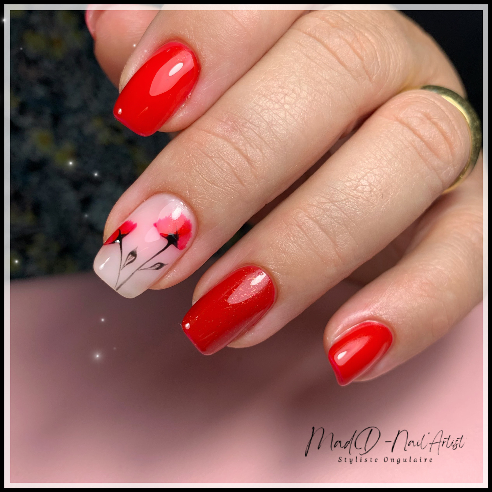 Manucure rouge brillante avec nail art floral aux coquelicots peints sur fond nude.